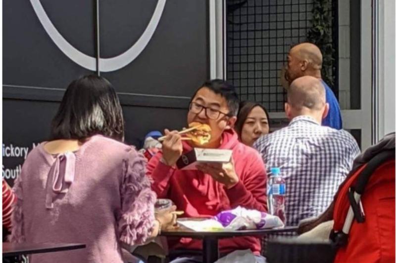 man eating burger with chopsticks