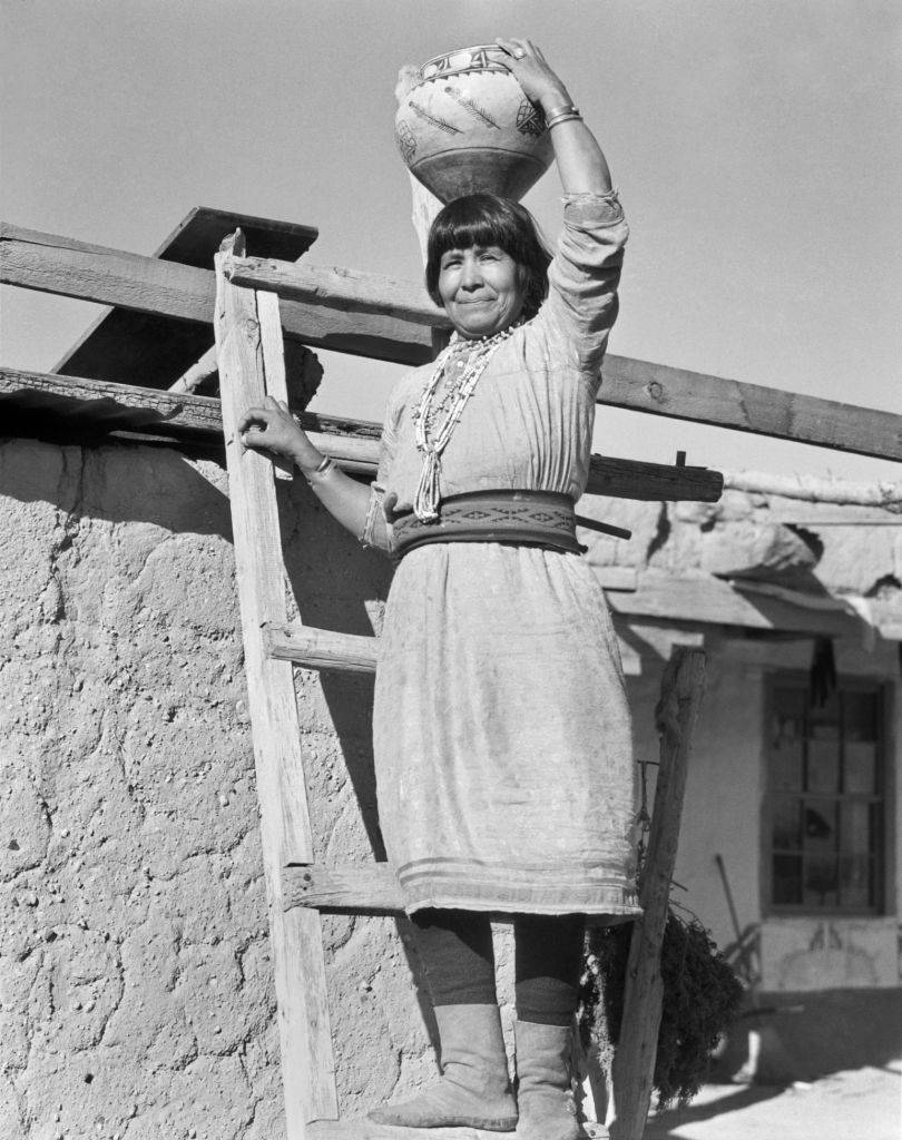 native american woman holding an olla while standing on a ladder