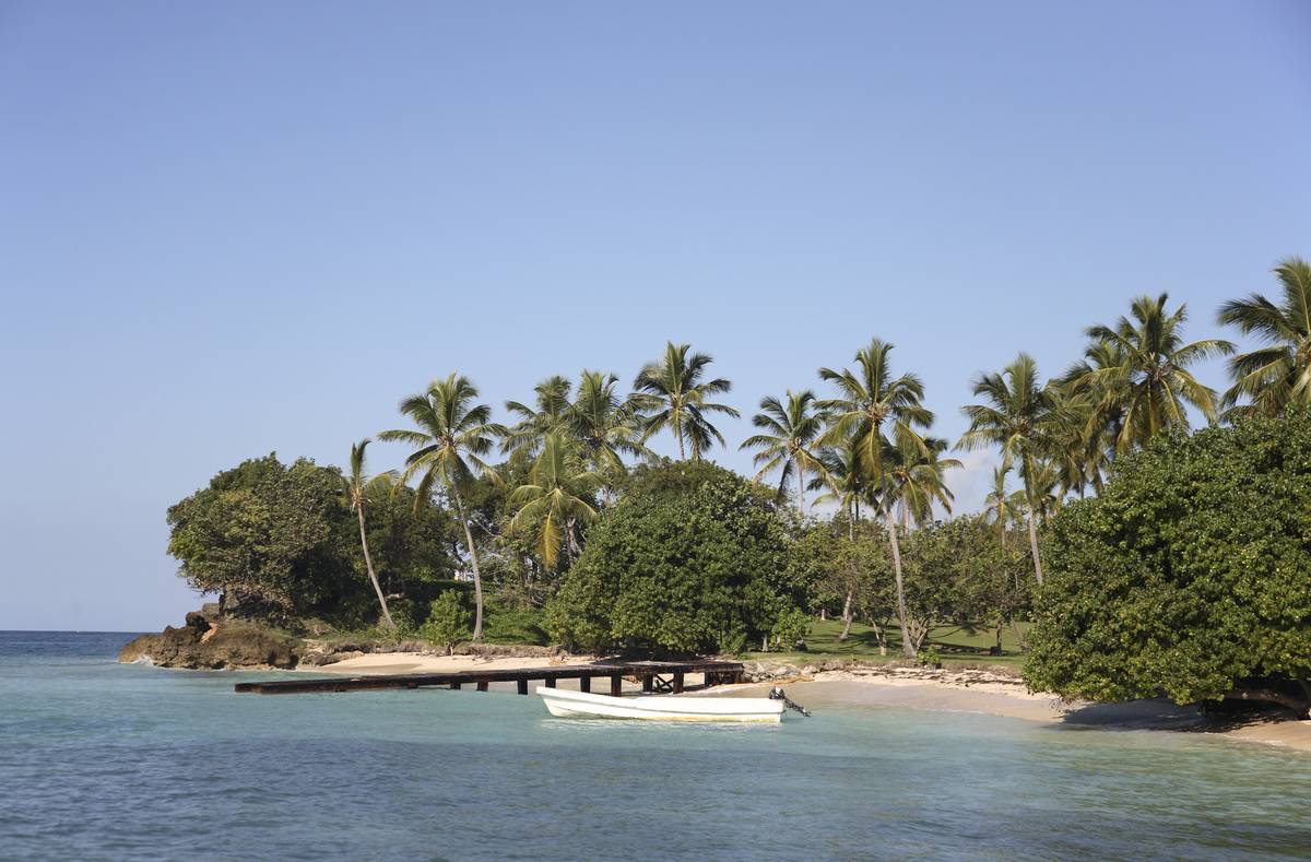 Dominican Republic, Samana Peninsula, Cayo Levantado, Bacardi island Palm tree lined shore wooden jetty and moored boat. 
