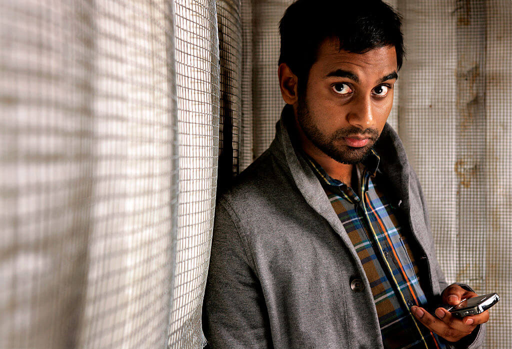 Aziz Ansari holds cellphone looks up at camera