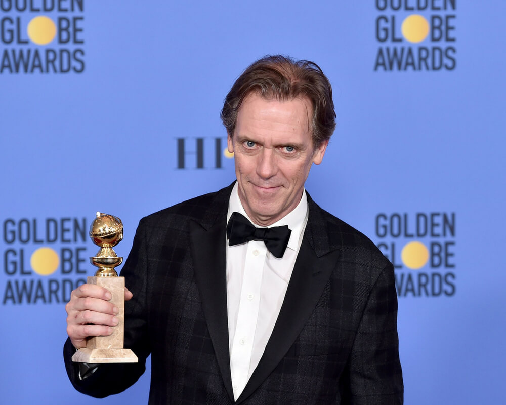 Hugh Laurie holds Golden Globe award while posing for photographers