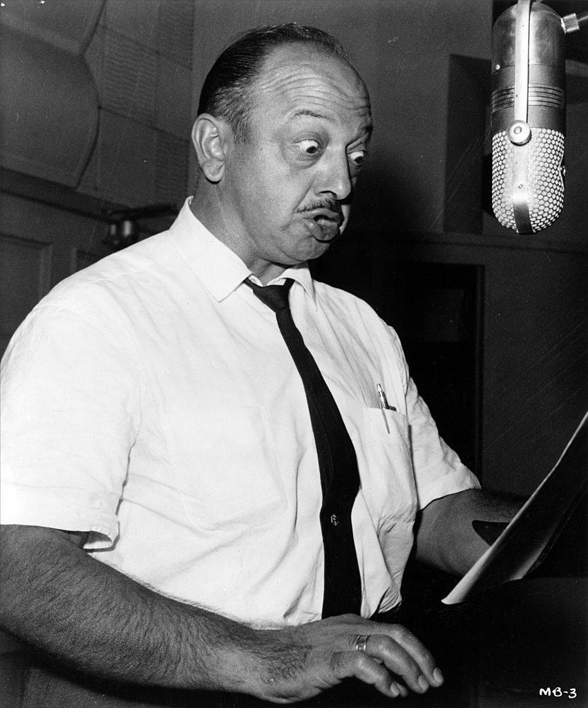 Mel Blanc speaking into hanging microphone while recording in studio 