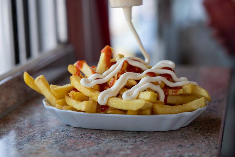 Mayonnaise is squeezed on fries with ketchup.