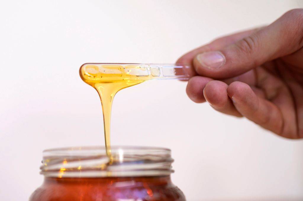 A man shows honey with a plastic stick