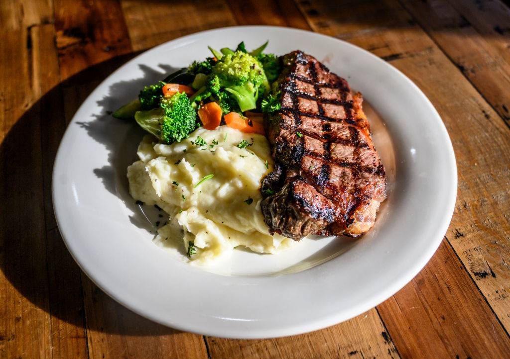 a plate of grilled shell steak with mashed potatoes and sauteed vegetables