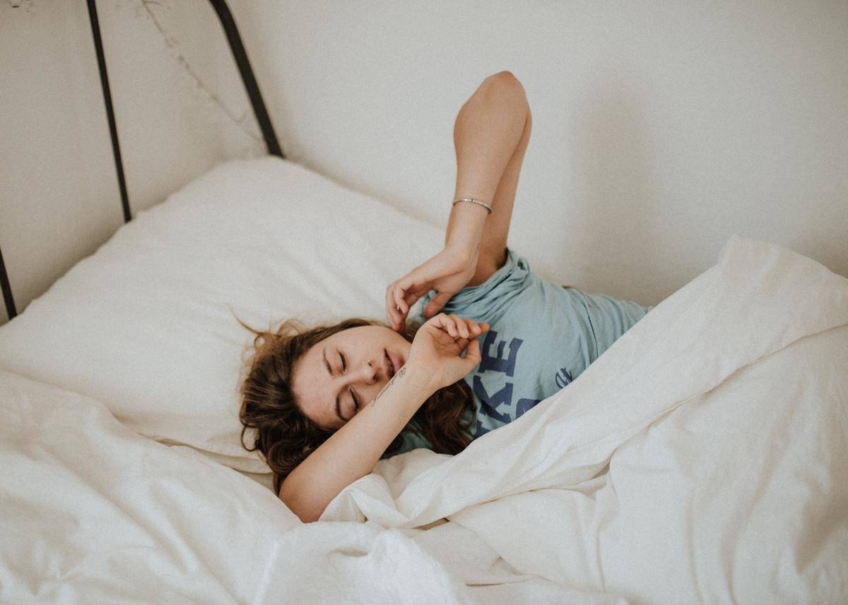woman in T-shirt waking up while laying in white bed