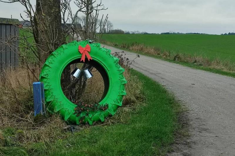 tractor tire painted green with red bow to look like wreath at the side of road