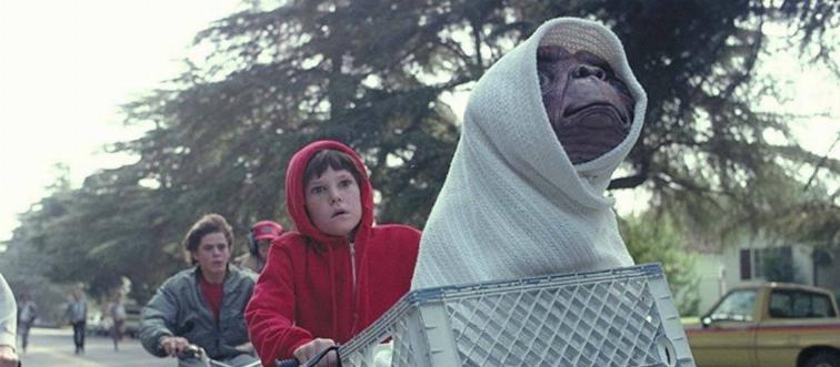 Henry Thomas riding bike as Elliott with E.T. in basket wrapped up in blanket in E.T. The Extra-Terrestrial