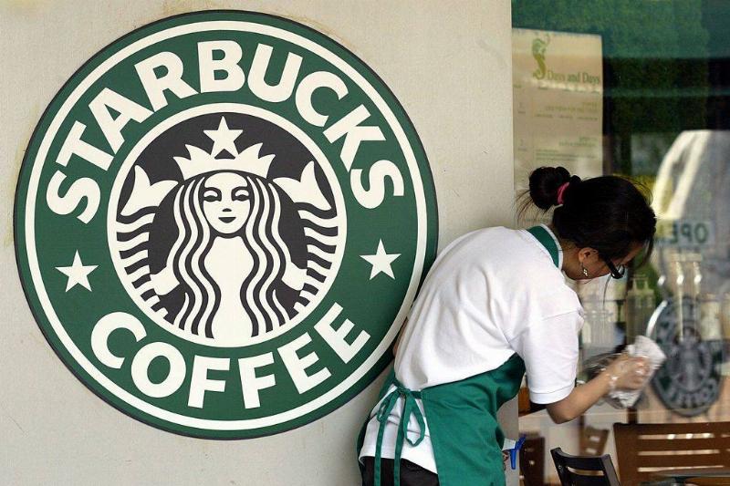 starbucks 71087266 A Starbucks worker cleans the window next to a company logo at a coffee store