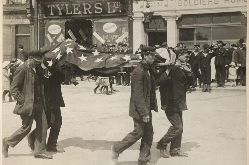 Four men carry the American flag-covered cover the body of victim  recovered from the RMS Lusitania as it is carried past saluting military
 and members of the public on the way to a temporary morgue, Queenstown 
(later known as Cobh), Ireland, May 1915.