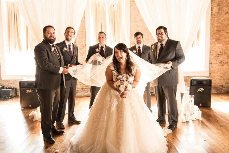 Bride holding flowers and beaming as groomsmen hold her train