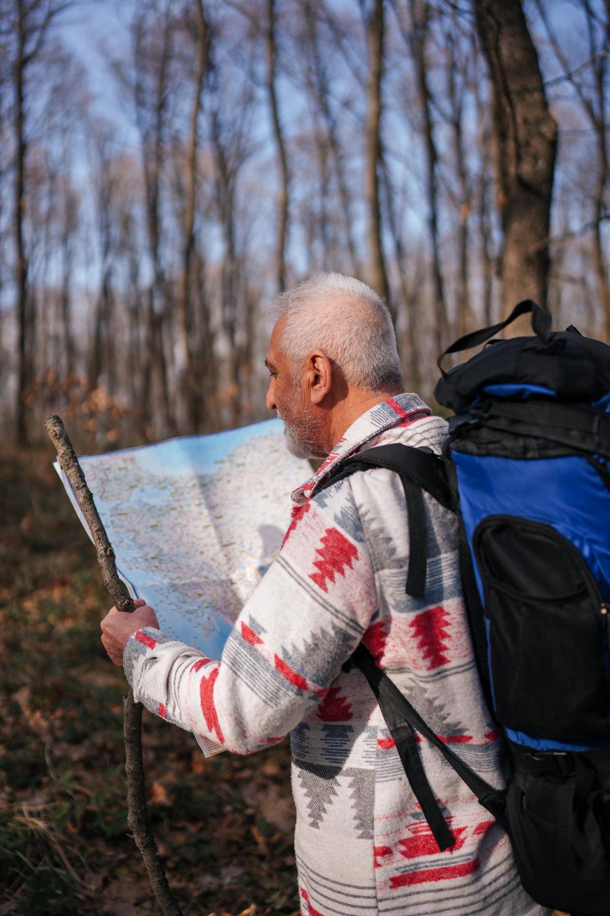 Man with walking stock holding peper map in woods