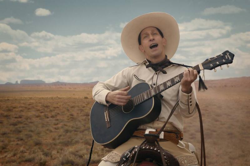 Tim Blake Nelson riding horse playing guitar and singing in white cowboy outfit in The Ballad of Buster Scruggs