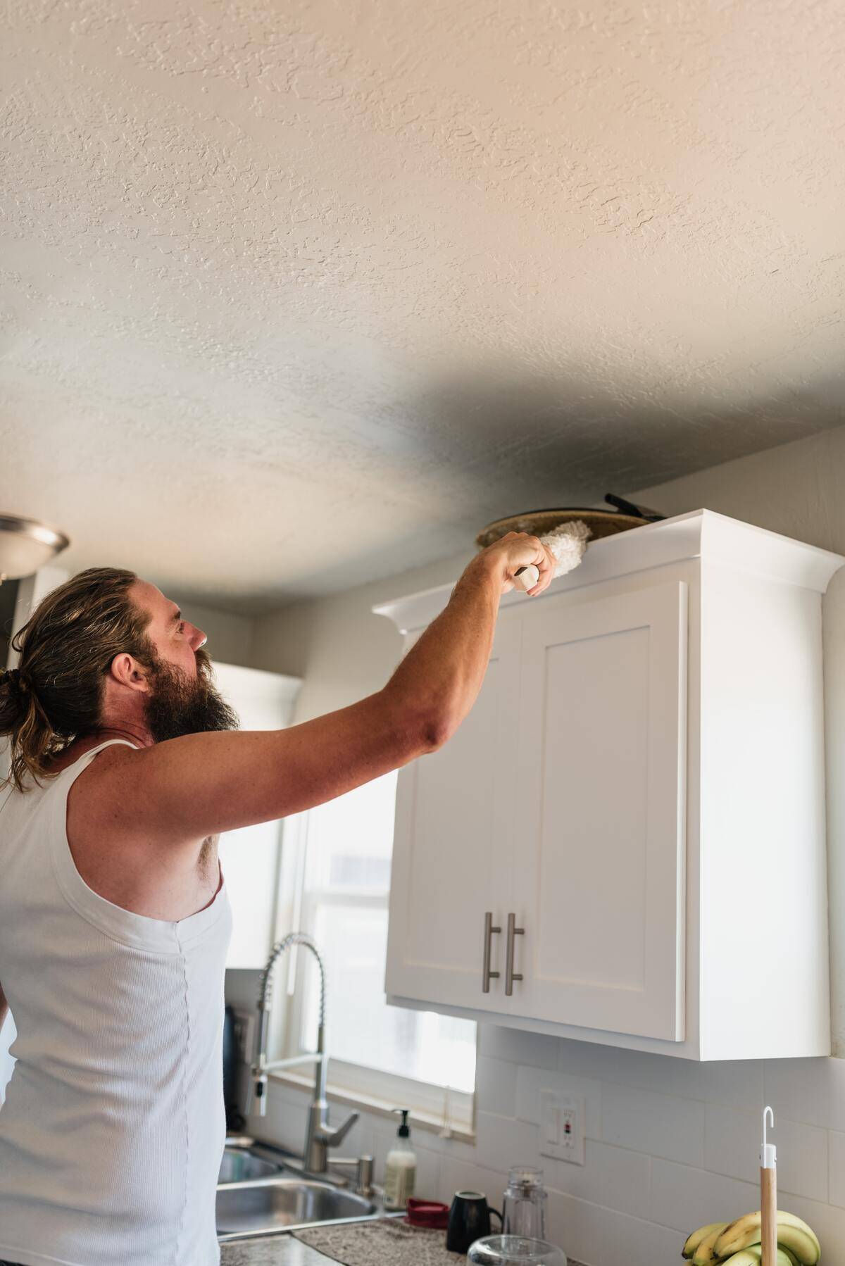bearded man dusting cabinet tops in kitchen