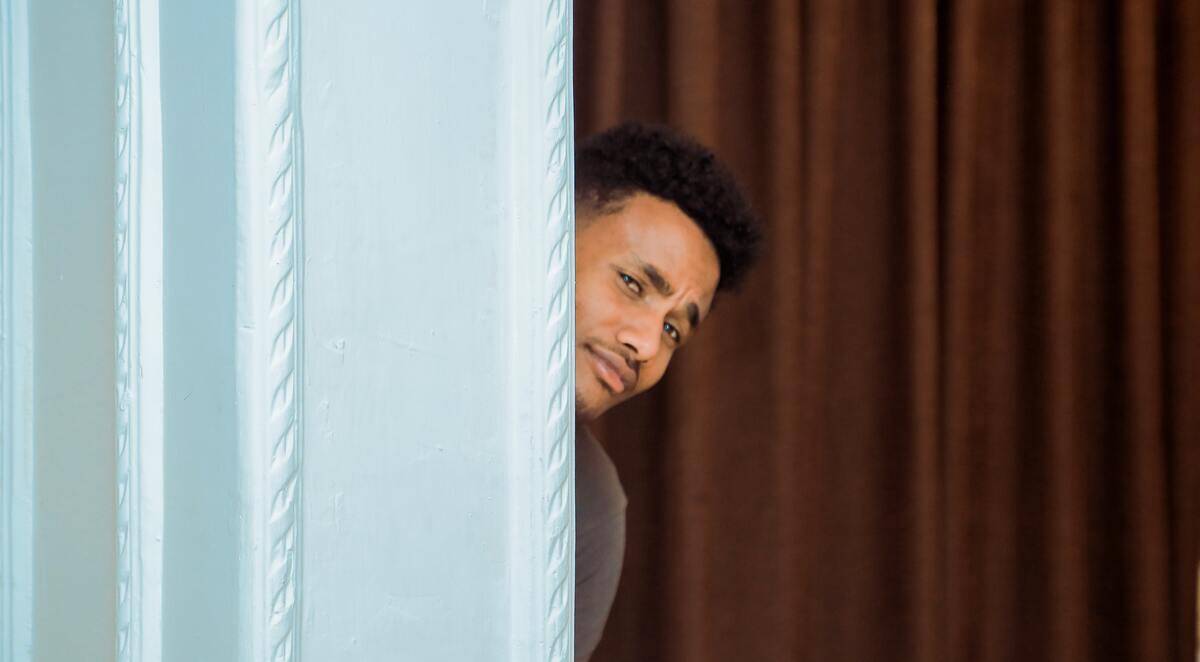 man peeking around corner with incredulous facial expression