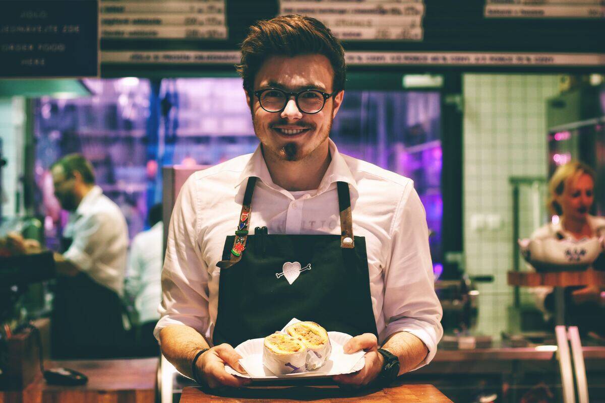 waiter smiling as he holds plate with sandwich in restaurant