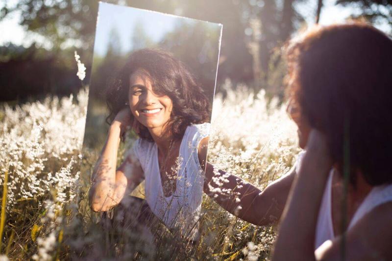 woman admiring herself in mirror among flowers