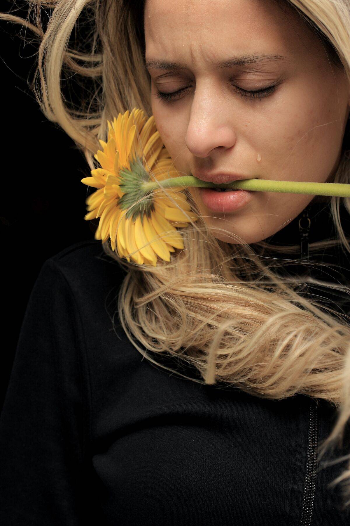 woman crying while holding sunflower in her mouth