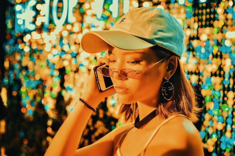 woman in baseball cap talking into phone while orange light shines on her