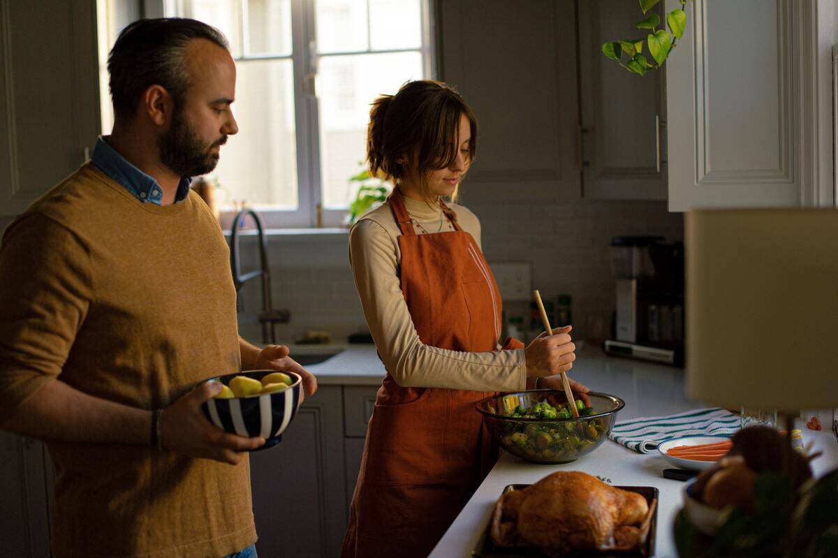 woman stirring salad while man holds bowl of food