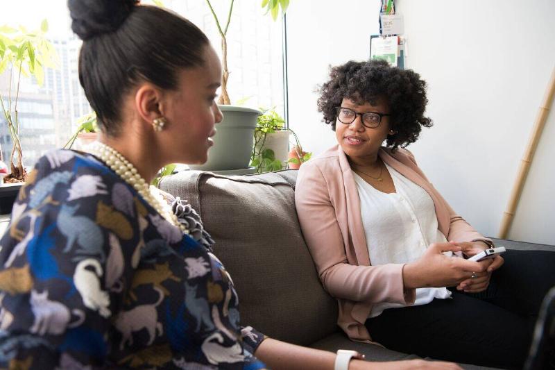 woman talking to another woman on couch holding phone