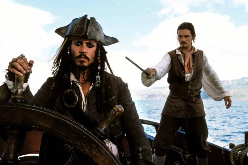 Johnny Depp steers ship as Captain Jack Sparrow in Pirates of the Caribbean The Curse of the Black Pearl while Orlando Bloom points sword as Will Turner