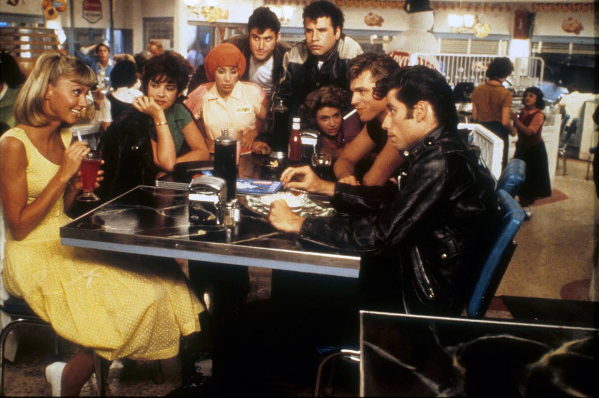 The cast of Grease sitting around malt shop table
