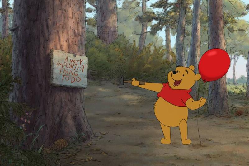 Winnie The Pooh happily pointing to sign while holding red balloon