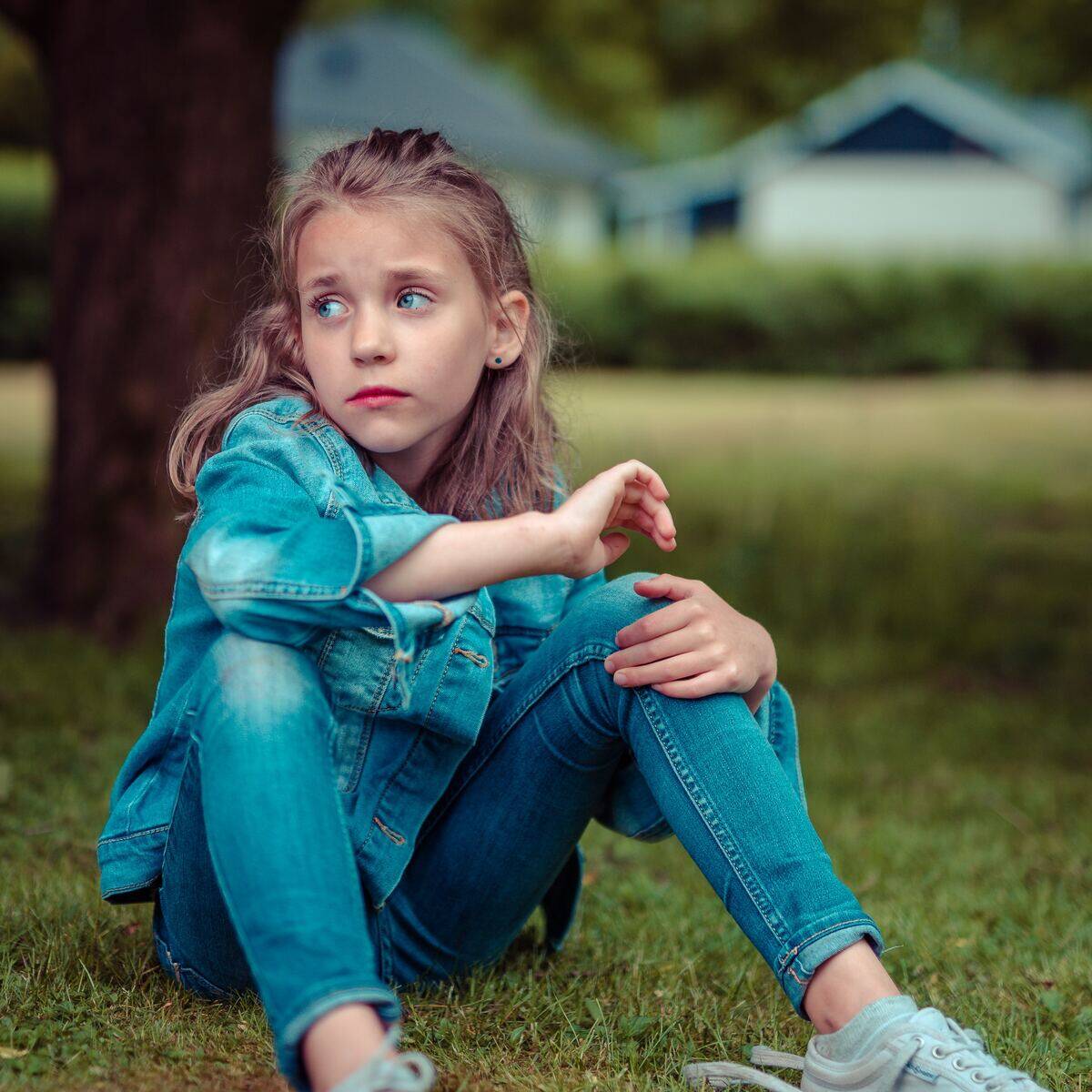 little girl looking worried while sitting on grass in front of tree