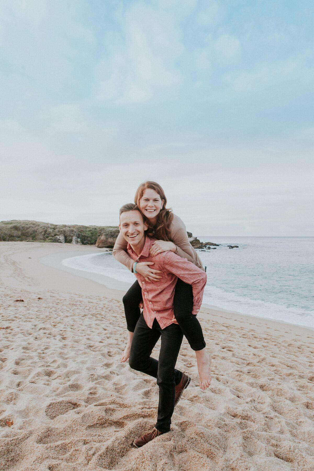 man giving woman piggy-back ride at beach