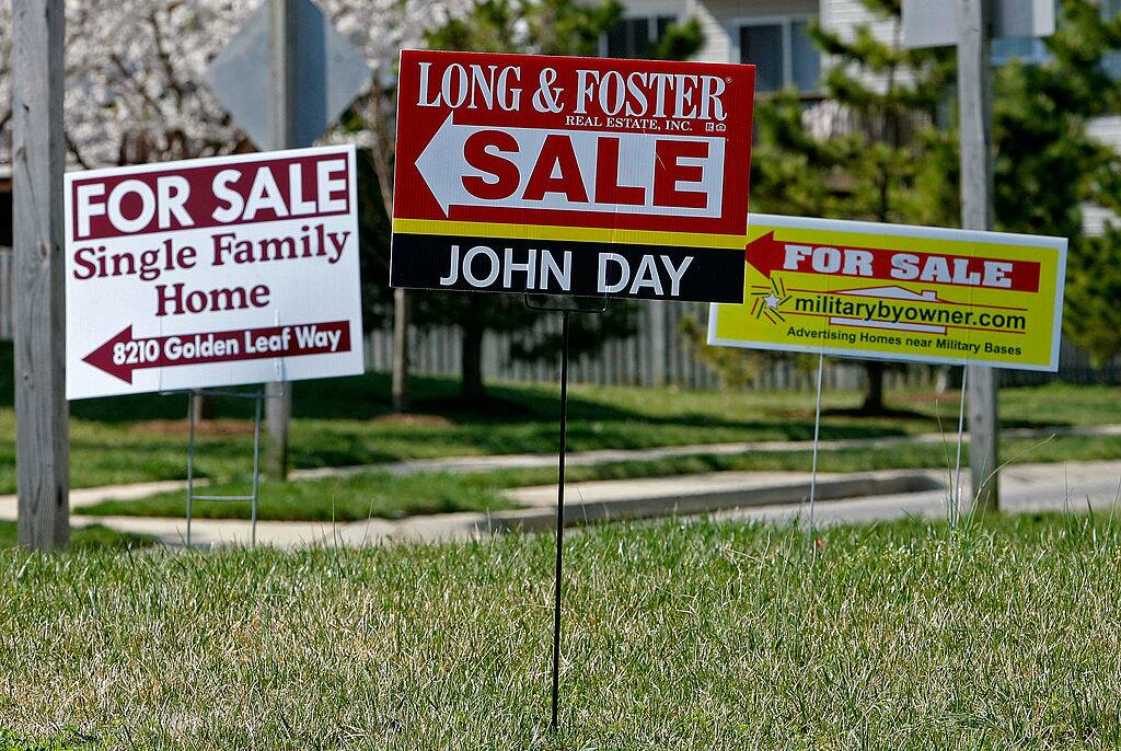 For sale signs stand on a medium strip in a housing development