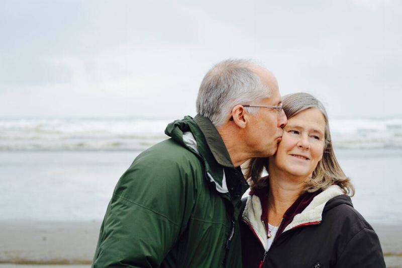 older man kissing older woman's cheek at beach