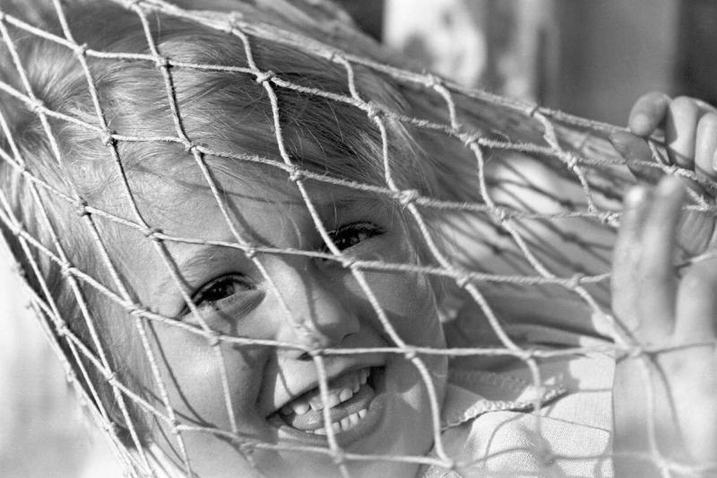 Small child smiling through the netting of a hammock, c.1930s. Small child smiling through the netting of a hammock, c.1930s.