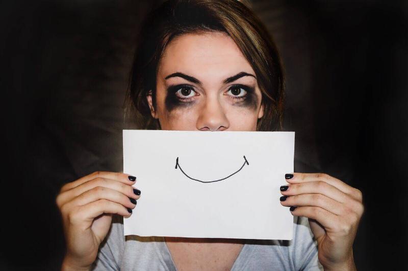 woman with running mascara holding up smile drawn on paper