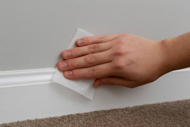 Hand wiping a dryer sheet on baseboards.