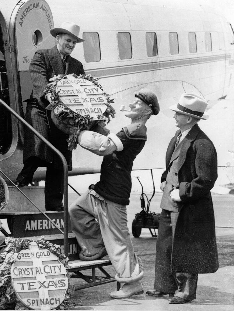 E.C. Segar, a man dressed as Popeye and B.H. Holsomback standing next to an aircraft