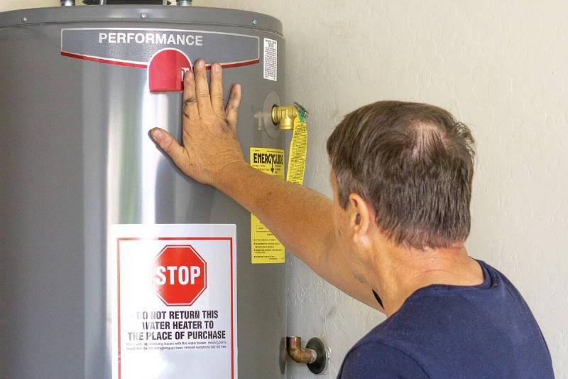 adult-male-with-hand-on-newly-installed-hot-water-2025-01-10-15-15-48-utc Man looking at label on water heater.
