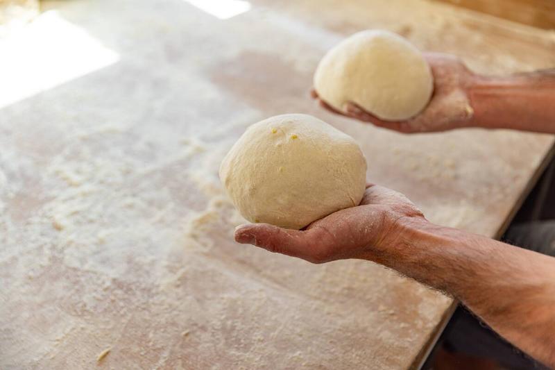 Man off-screen holding two piles of pizza dough