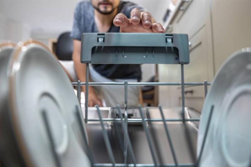 close-up-of-a-man-pulls-out-clean-dishes-from-the-2025-03-18-15-01-14-utc Man reaching into dishwasher to clear dishes.