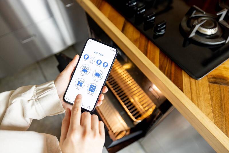 controlling-kitchen-appliances-with-a-smart-phone-2025-03-13-09-31-07-utc Woman using a phone to preheat the oven.