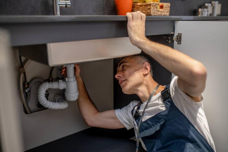 man-carefully-examining-bottom-of-sink-and-pipe-2024-10-18-04-54-31-utc Plumber installing a garbage disposal.