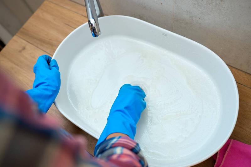 Gloved hands cleaning a white sink.