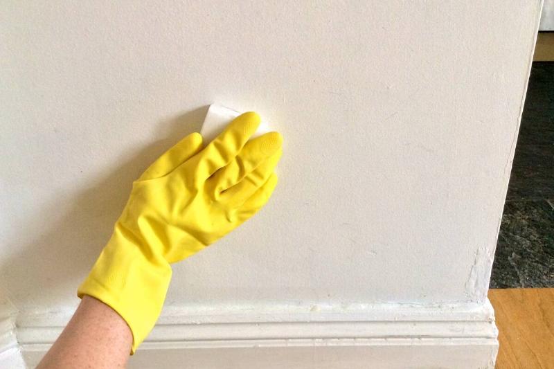 A cleaner's hand in a yellow glove cleaning a wall.
