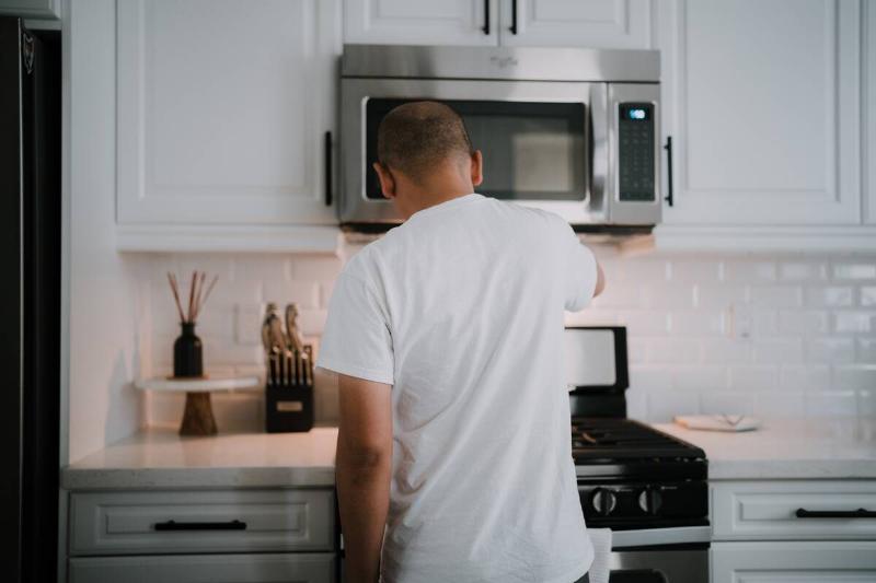 young-man-cooking-in-kitchen-at-home-bright-modern-2024-12-06-01-40-28-utc Man cooking in front of over-range microwave.