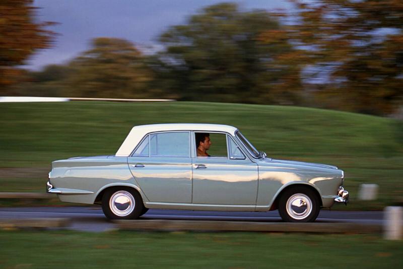 Man driving a Ford Cortina past a grassy hill