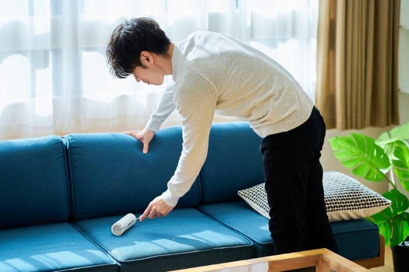 Man using lint roller on a couch. 