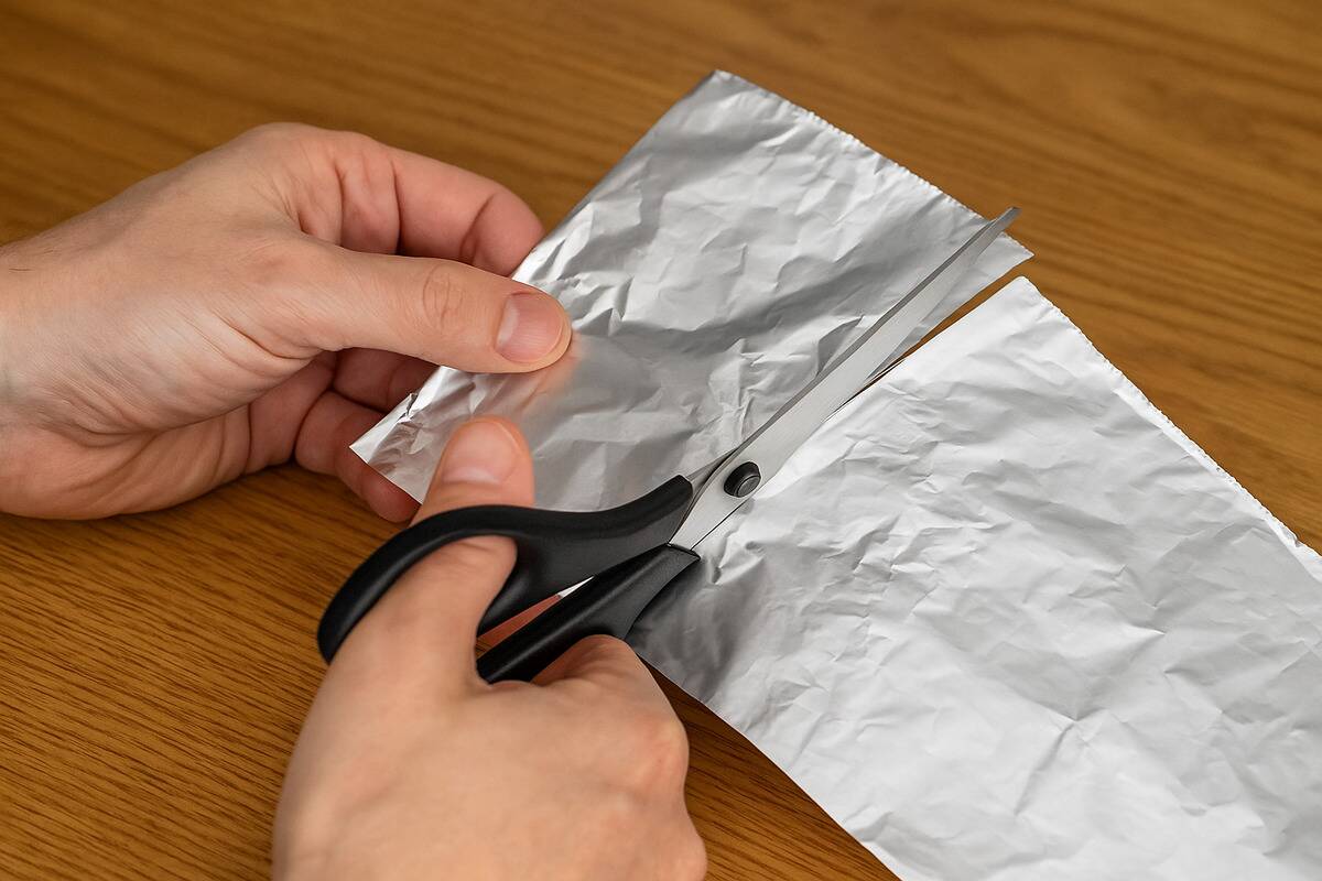 Hands cutting aluminum foil with scissors. 