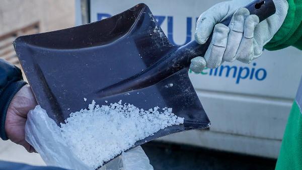 A person pouring salt in bag with shovel.