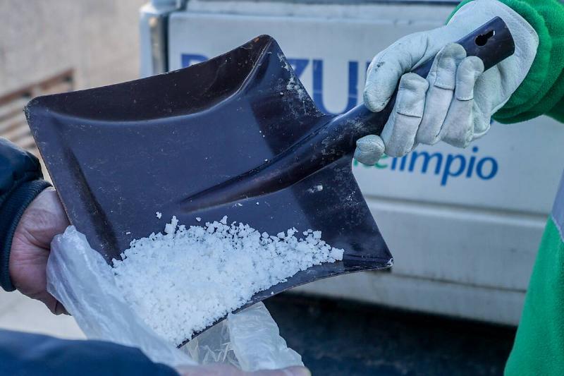 A person pouring salt in bag with shovel.