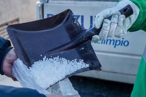 A person pouring salt in bag with shovel.